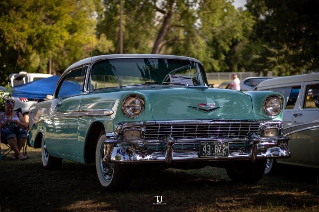A green and white vintage car is parked in the grass at a car show.