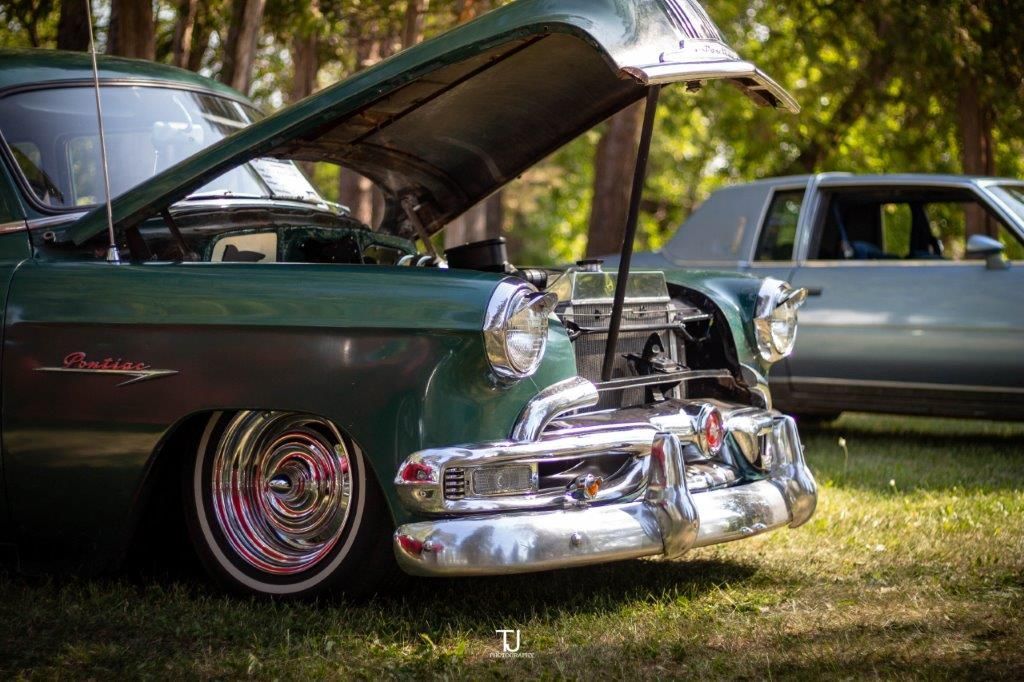 A green car with the hood up is parked in the grass.