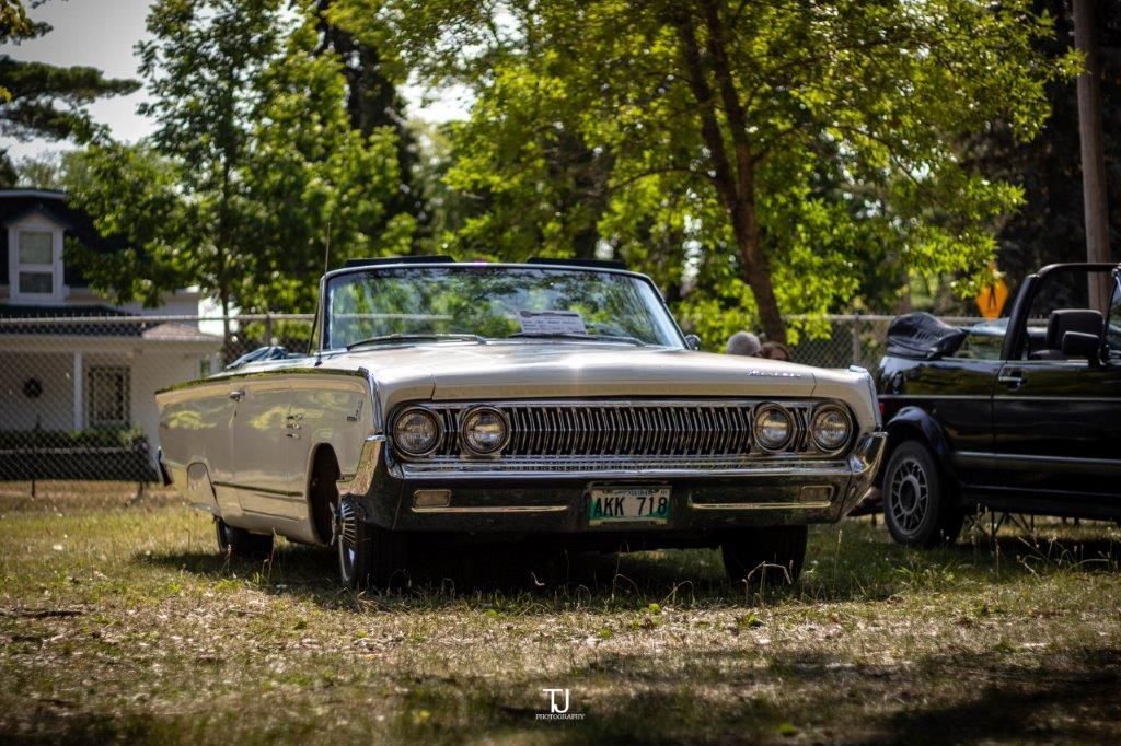 A white convertible car is parked in a grassy field next to a black truck.