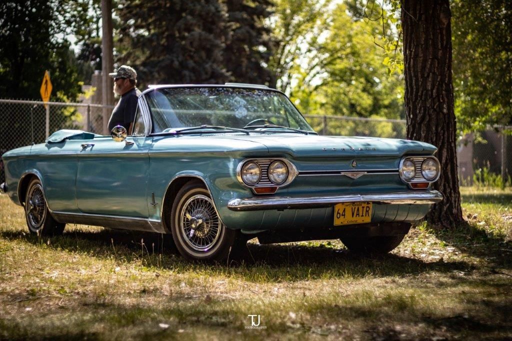 A man is sitting in a blue convertible car parked in a grassy field.