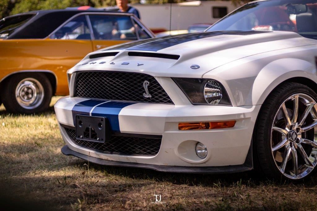 A white ford mustang is parked in a grassy field.