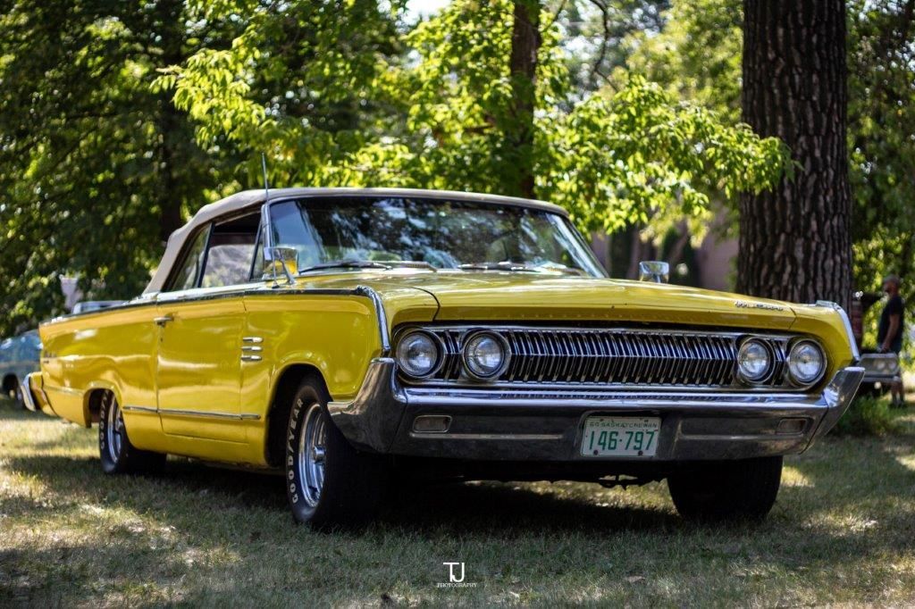 A yellow car is parked in the grass in front of a tree.