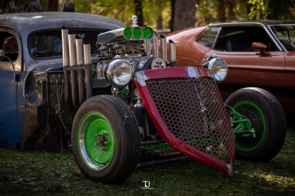 A red hot rod with green wheels is parked next to a brown car.