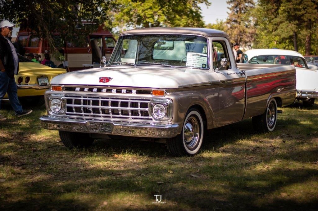 A silver pickup truck is parked in the grass at a car show.