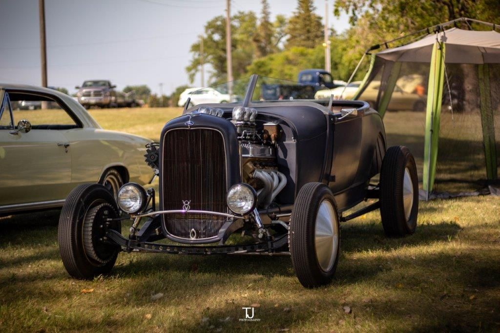 A black hot rod is parked in a grassy field next to a tent.
