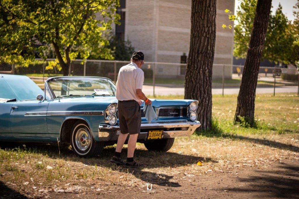 A man is standing next to a blue car in a park.