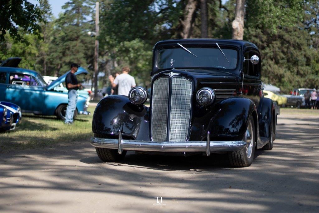 A black car is parked in a parking lot at a car show.