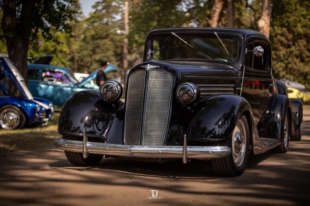 An old black car is parked in a parking lot at a car show.