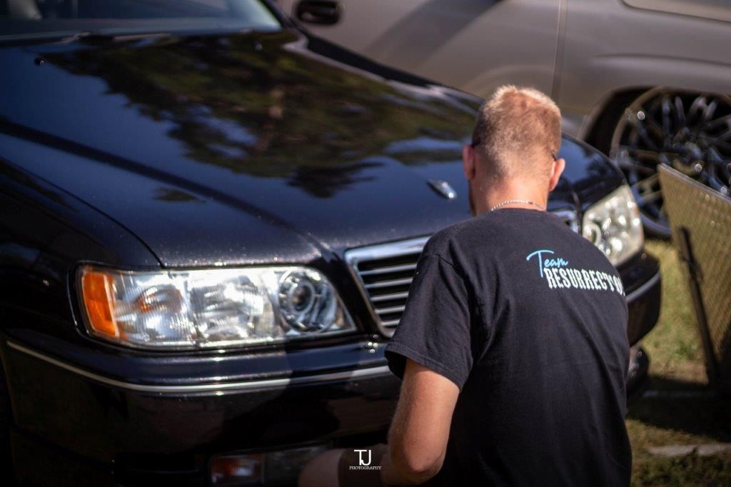 A man in a black shirt is standing in front of a black car.