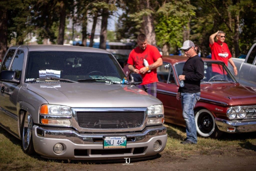 A man in a red shirt is standing next to a silver truck at a car show.