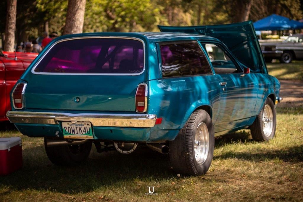 A blue station wagon with the hood up is parked in the grass.