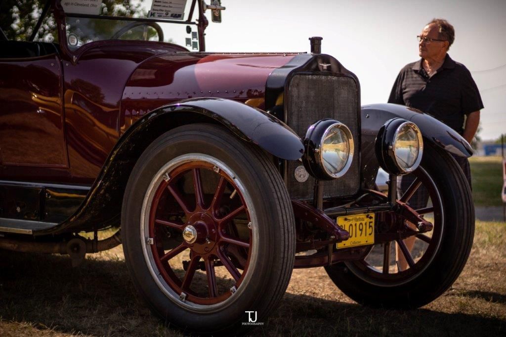 A man is standing next to an old car with a license plate that says yy 29