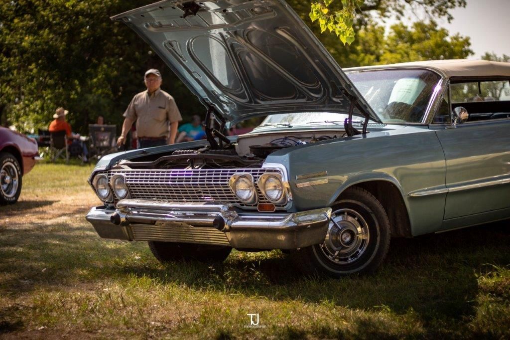 A man is standing next to an old car with the hood up.