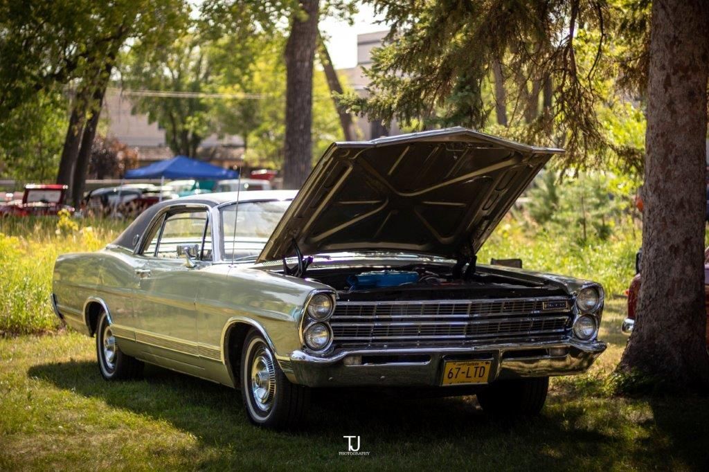 A silver car with the hood up is parked in the grass.