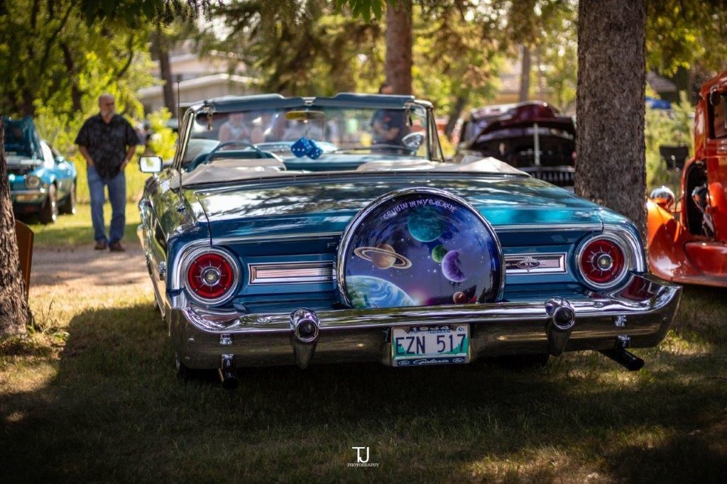 A blue convertible car is parked in the grass next to a tree.