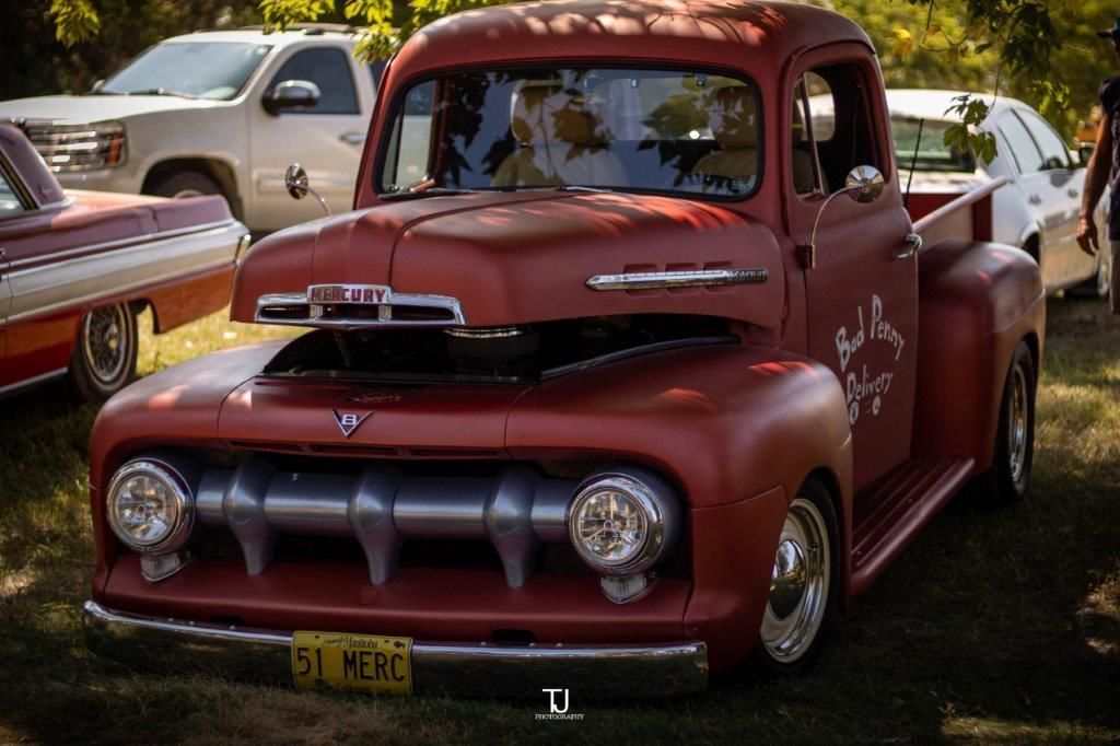 A red pickup truck is parked in a grassy field.