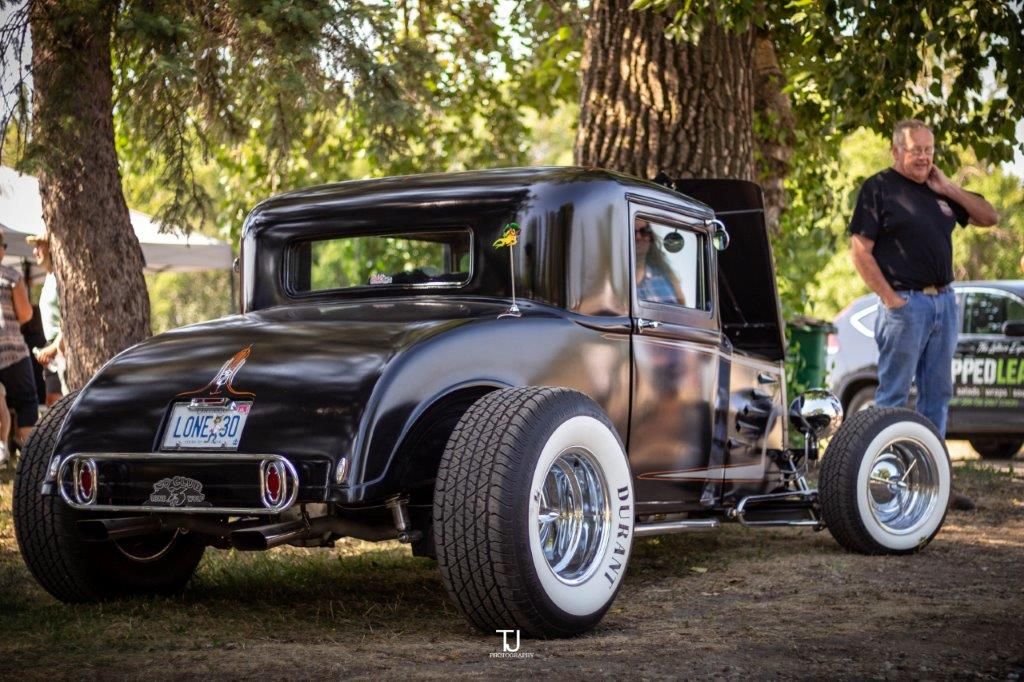 A man is standing next to a black car with white tires.