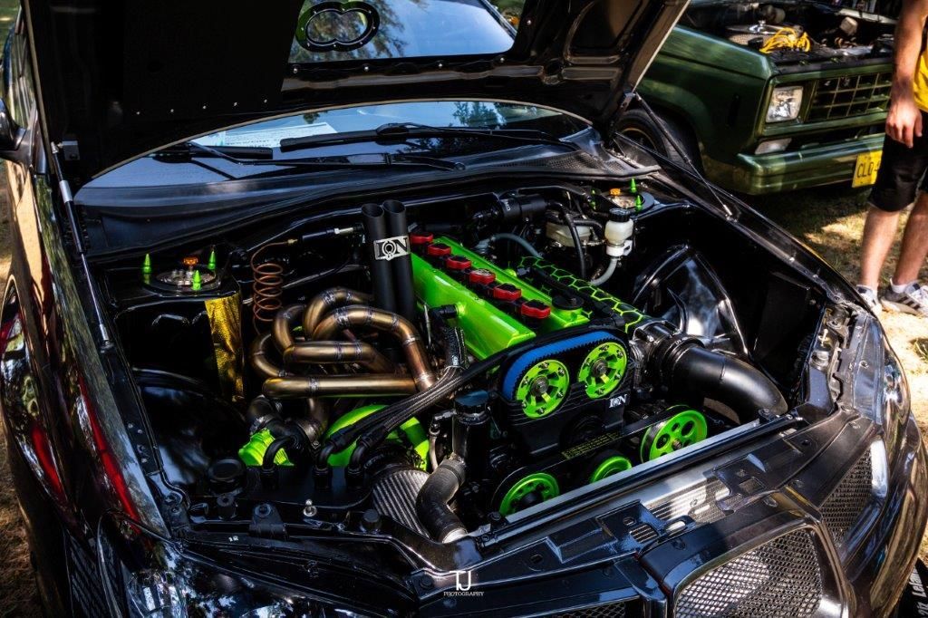 A black car with the hood open and a green engine.