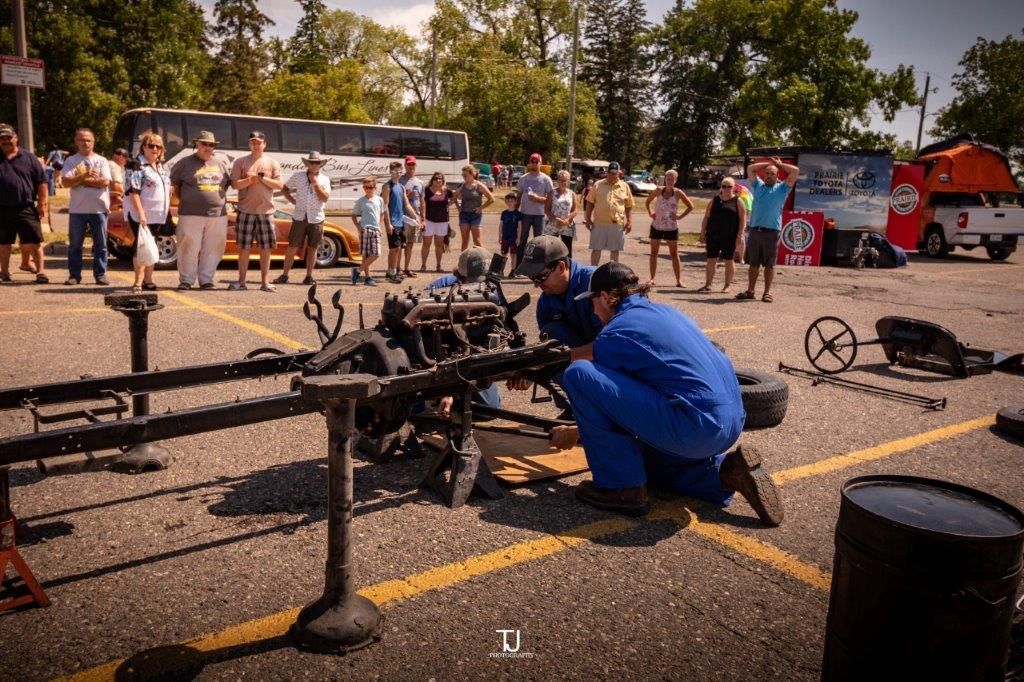 Two men are working on a car engine in a parking lot.