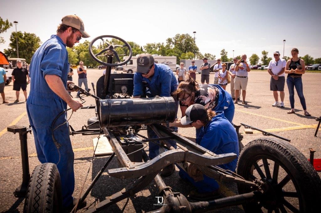 A group of men are working on an old car in a parking lot.