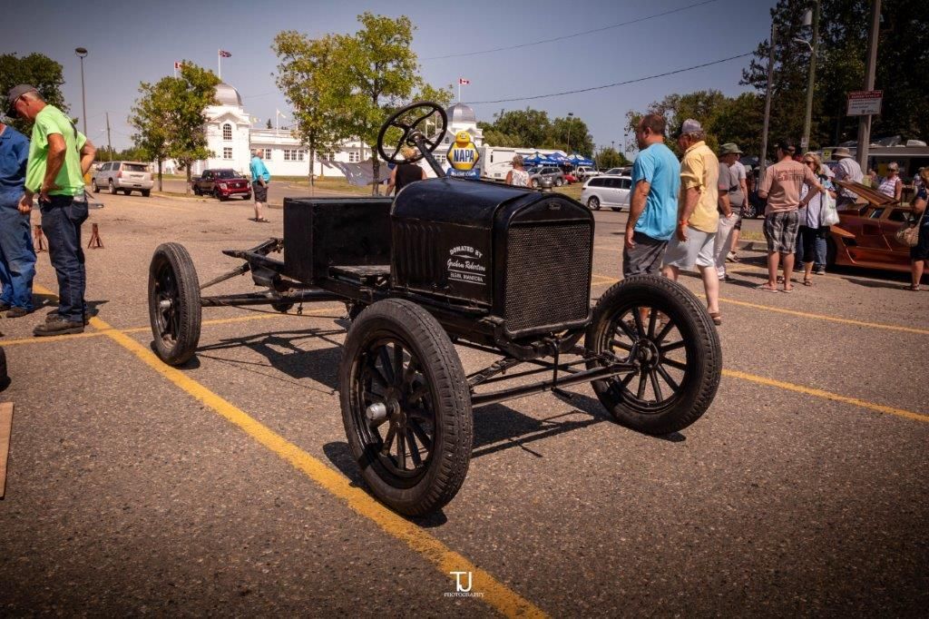 A group of people are standing around an old car in a parking lot.
