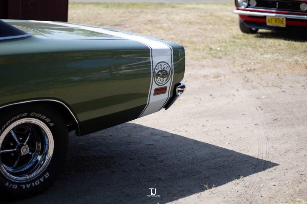 A green dodge charger is parked in a driveway next to a red mustang.
