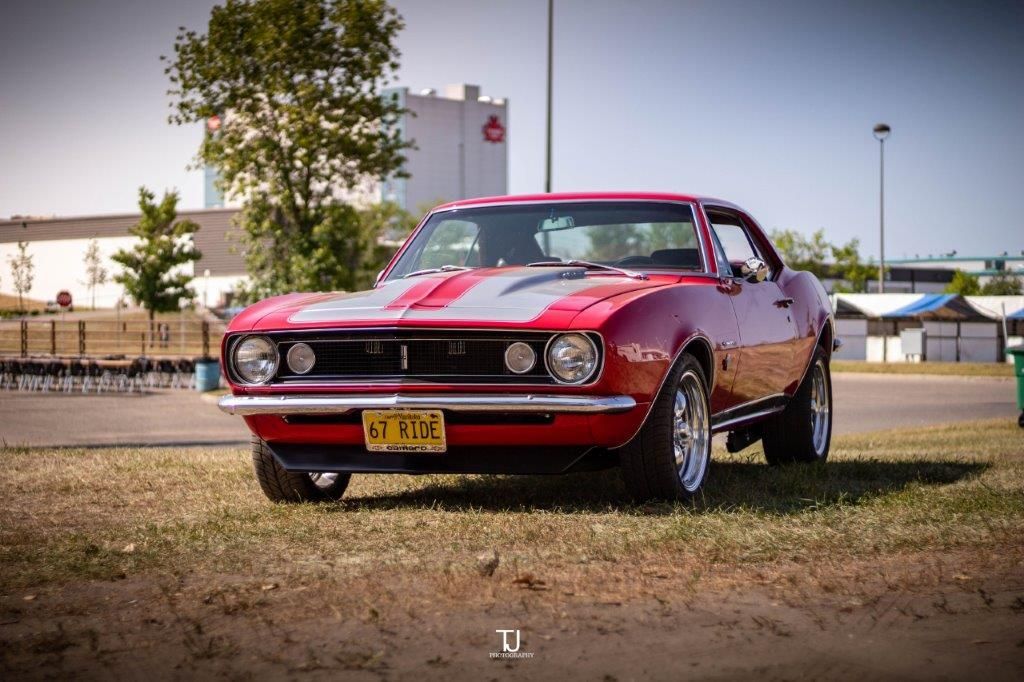 A red muscle car is parked in the grass in front of a building.