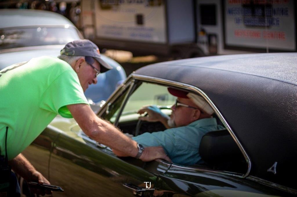 A man in a green shirt is talking to another man in a car.