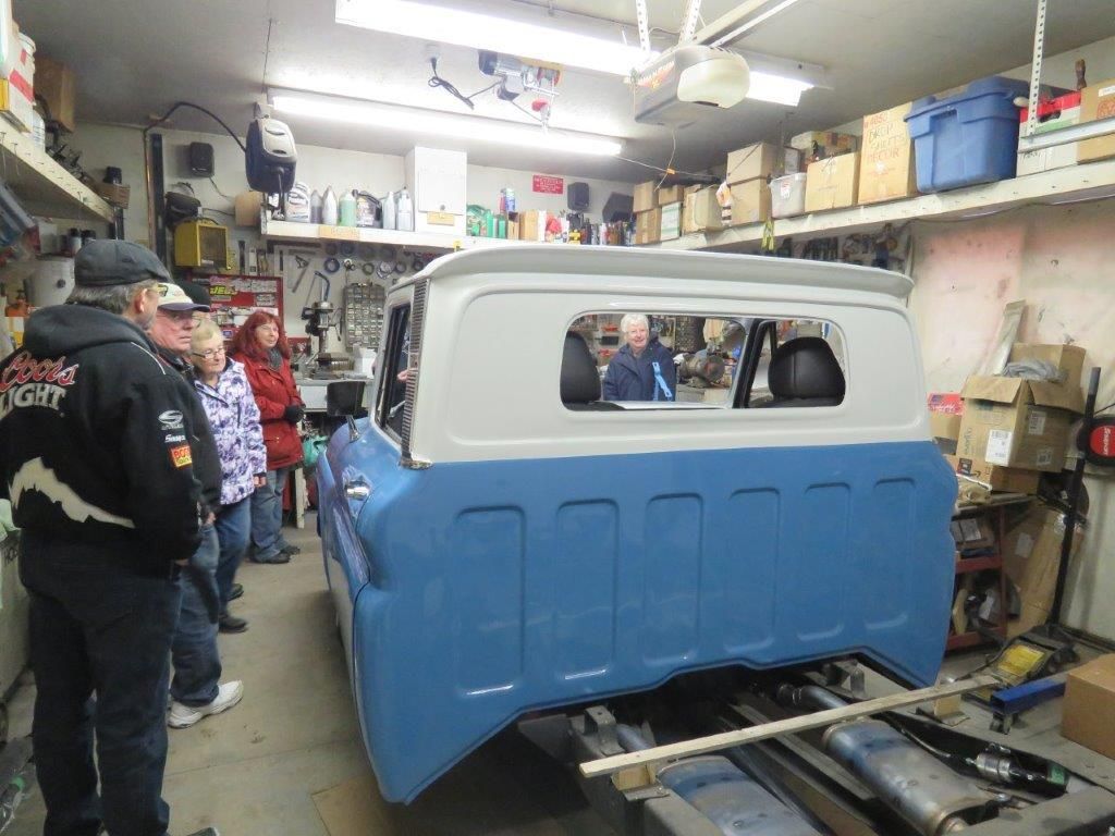 A group of people are standing around a blue and white truck in a garage.