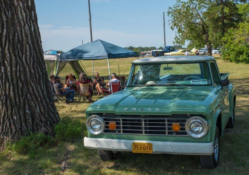 A green truck is parked in a grassy field next to a tree.