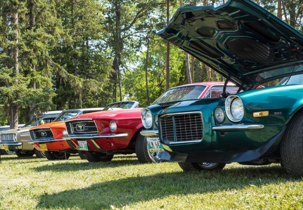 A row of old cars are parked in a grassy field with their hoods open.