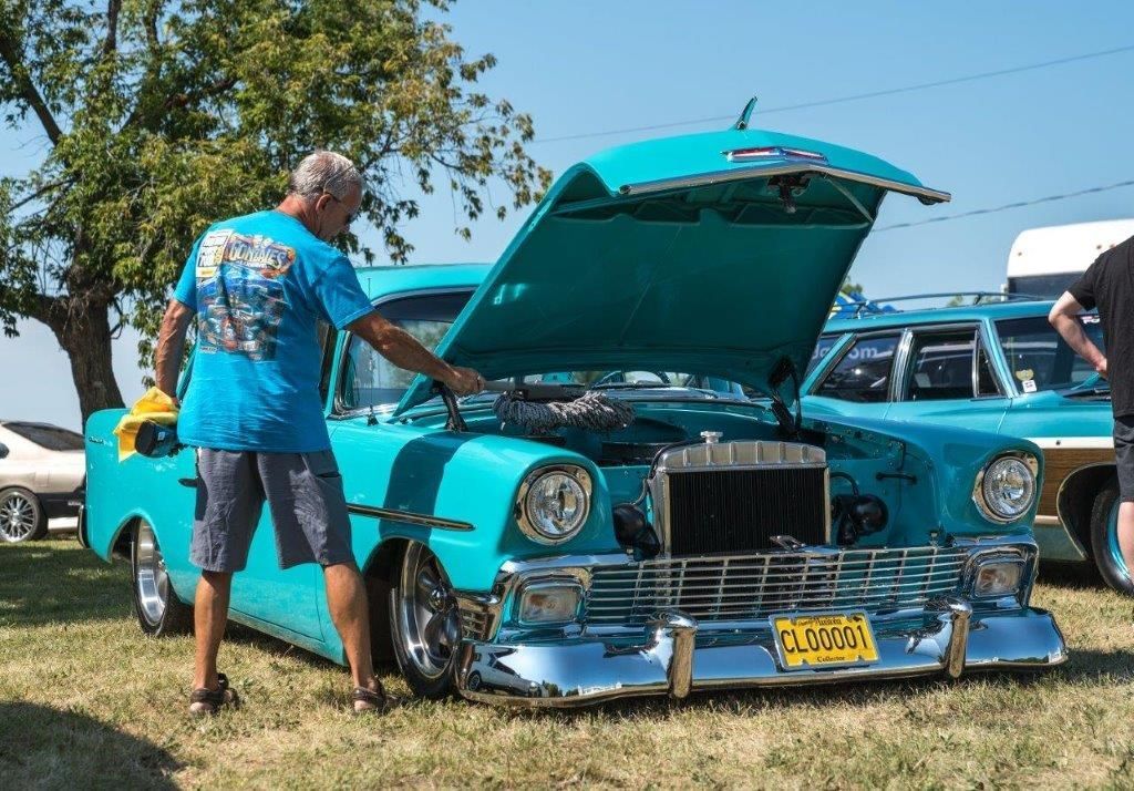 A man is looking under the hood of a blue car.