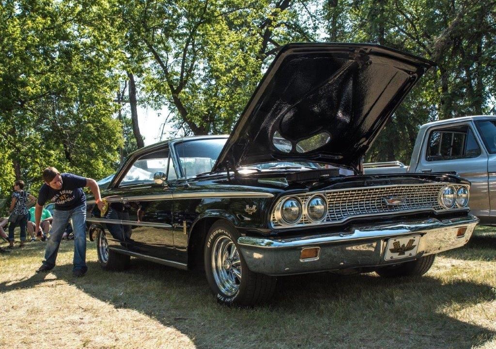 A man is standing next to a black car with the hood up.