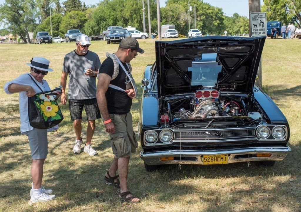 A group of people are looking under the hood of a car.
