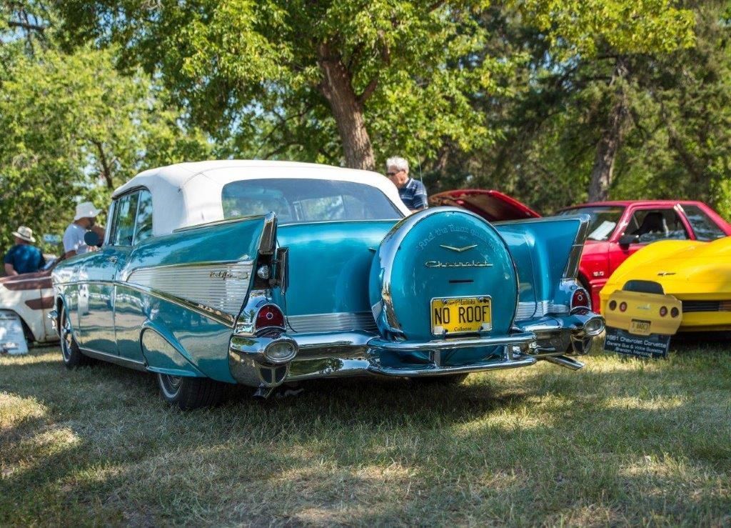 A blue and white car is parked in the grass at a car show.
