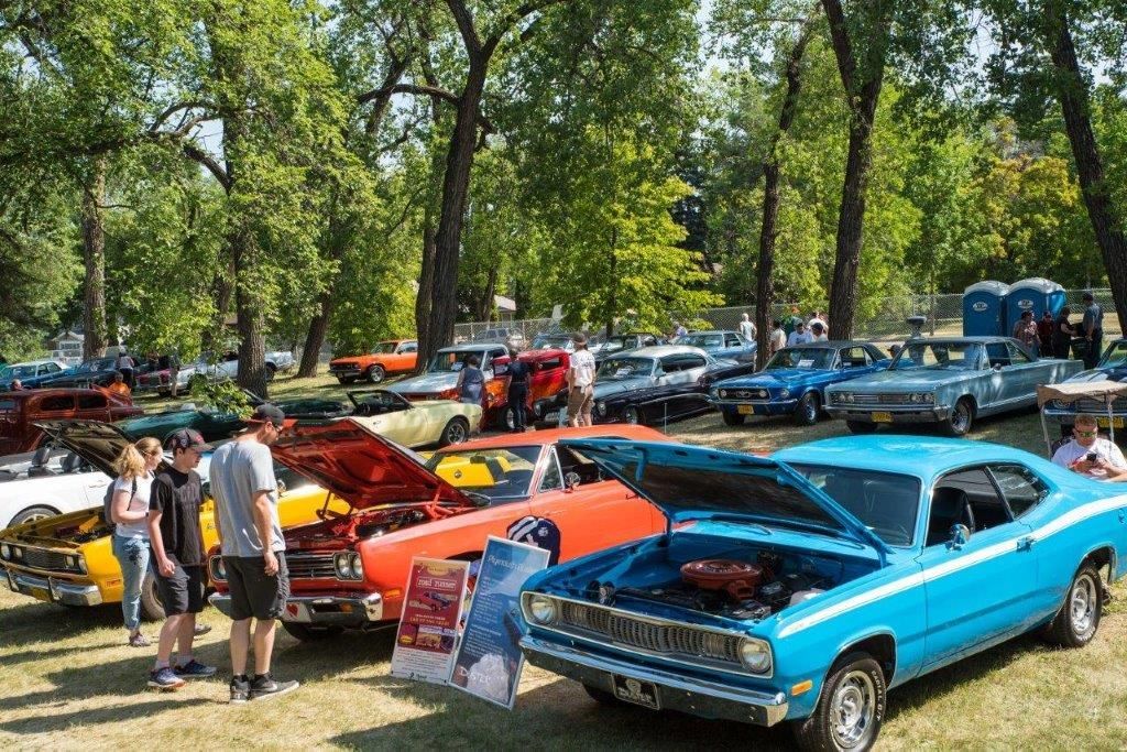 A group of people are standing around a row of cars at a car show.