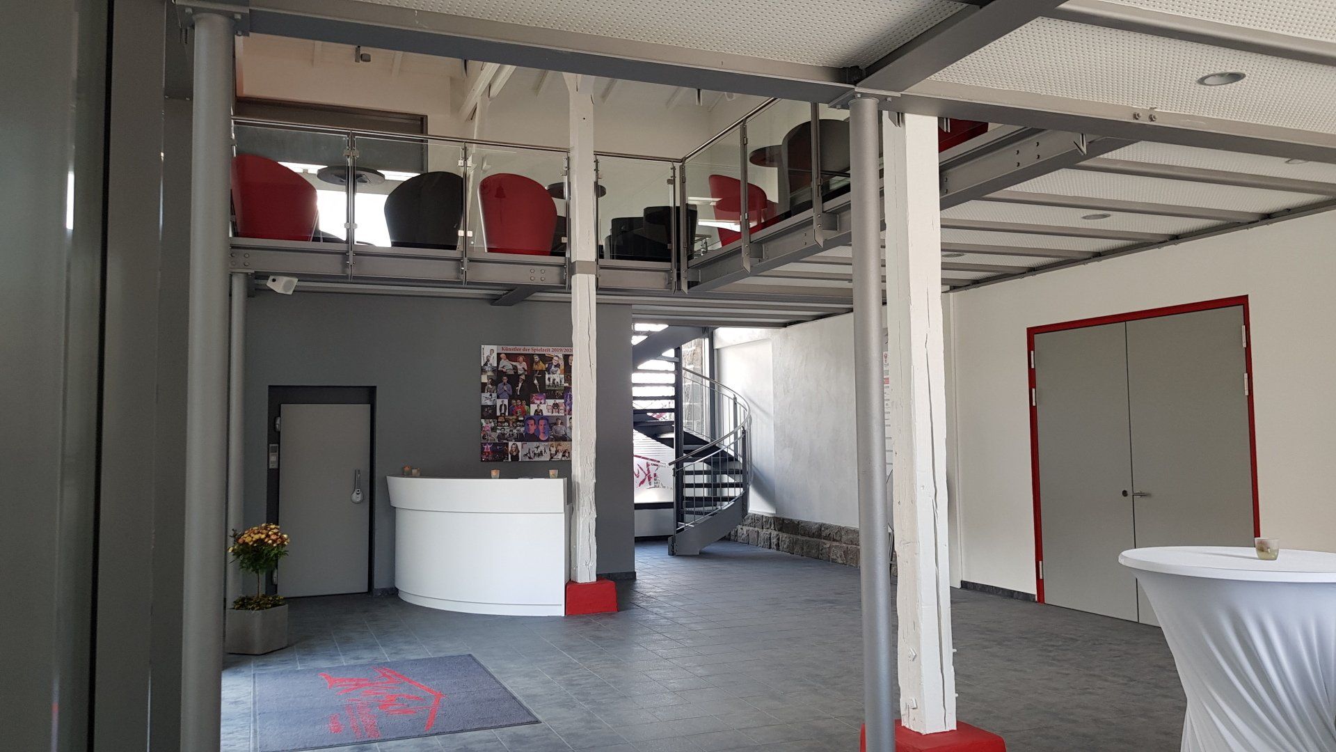 Moderne Lobby mit Rezeption, Wendeltreppe, Lounge-Bereich im Zwischengeschoss mit Stühlen und weißen Säulen.