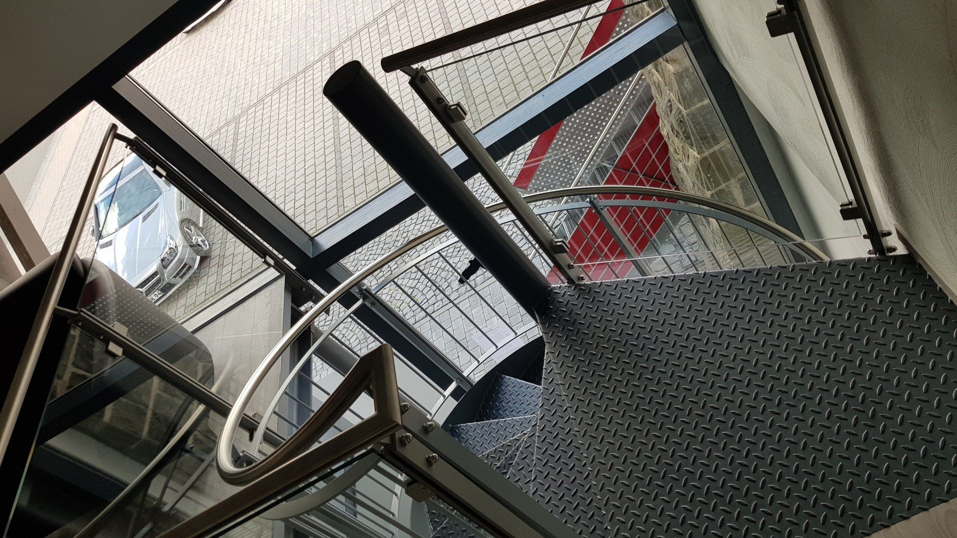 Draufsicht auf eine dunkle Metallwendeltreppe mit Sicherheitsgeländer, gesehen durch ein großes Glasfenster.