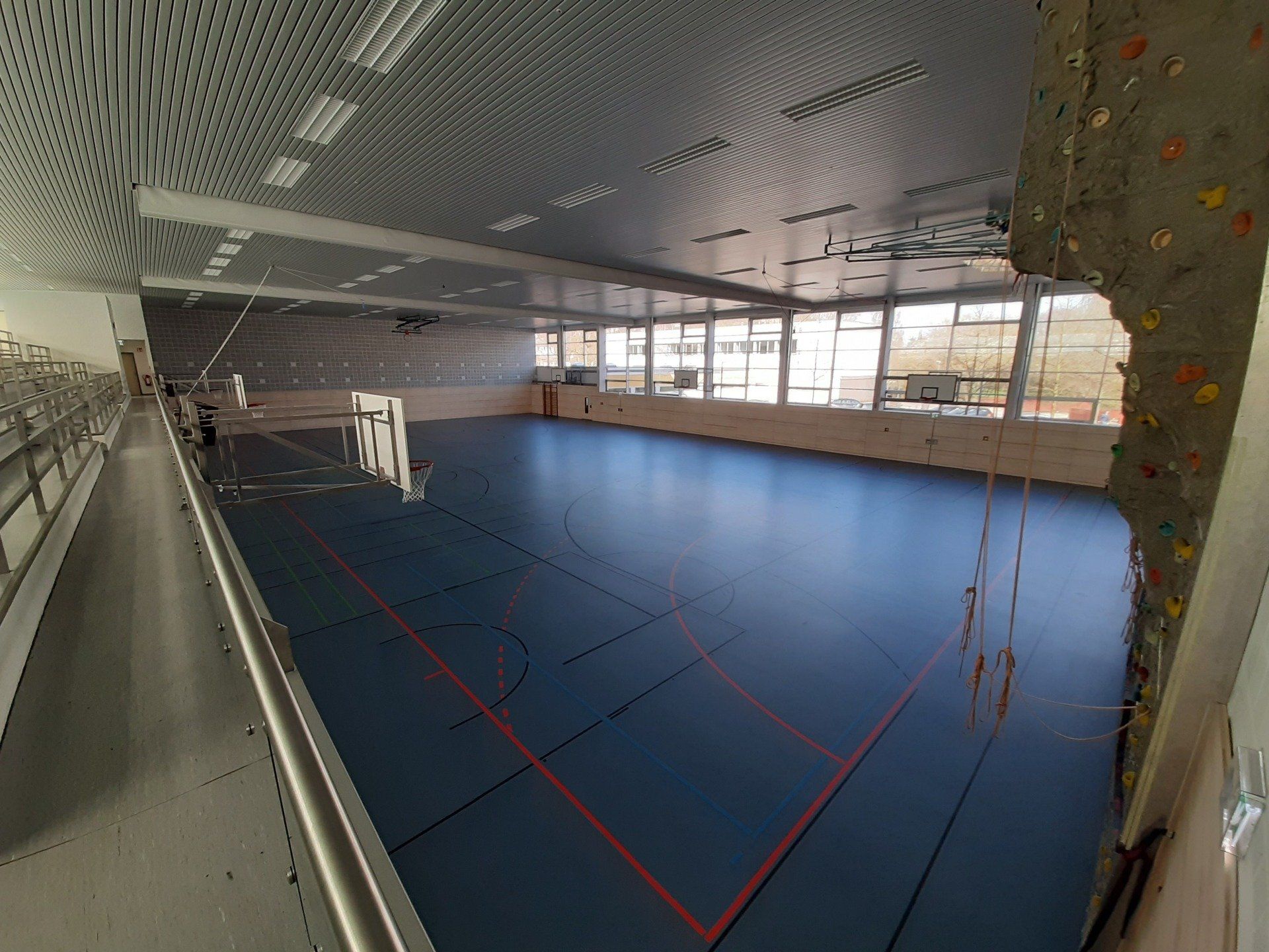 Eine Sporthalle mit blauem Boden, Spielfeldlinien, einer Kletterwand auf der rechten Seite