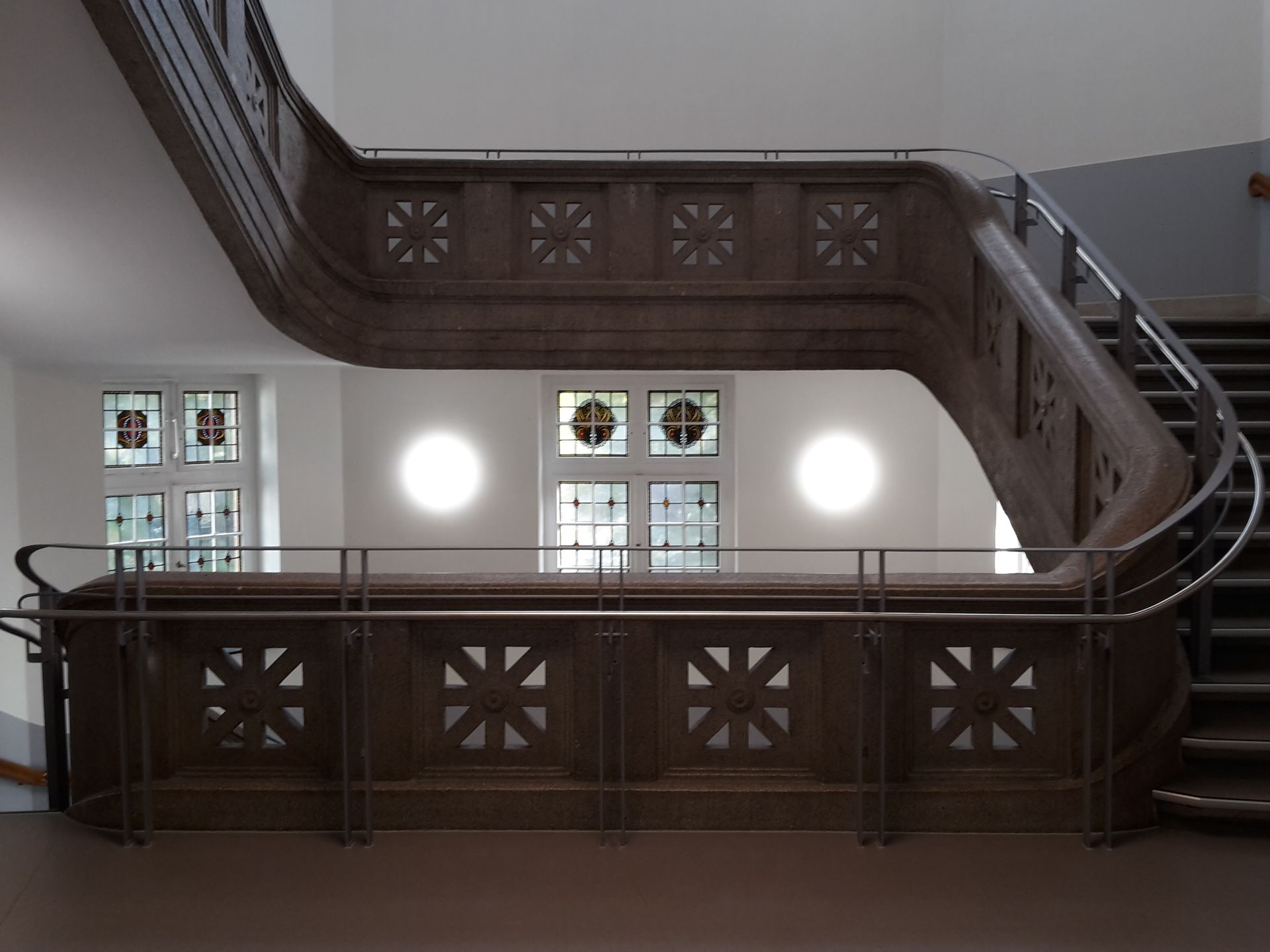 Eine moderne Treppe mit hölzernem Geländer in Sternform und Metallgeländer in einem hell erleuchteten Flur.