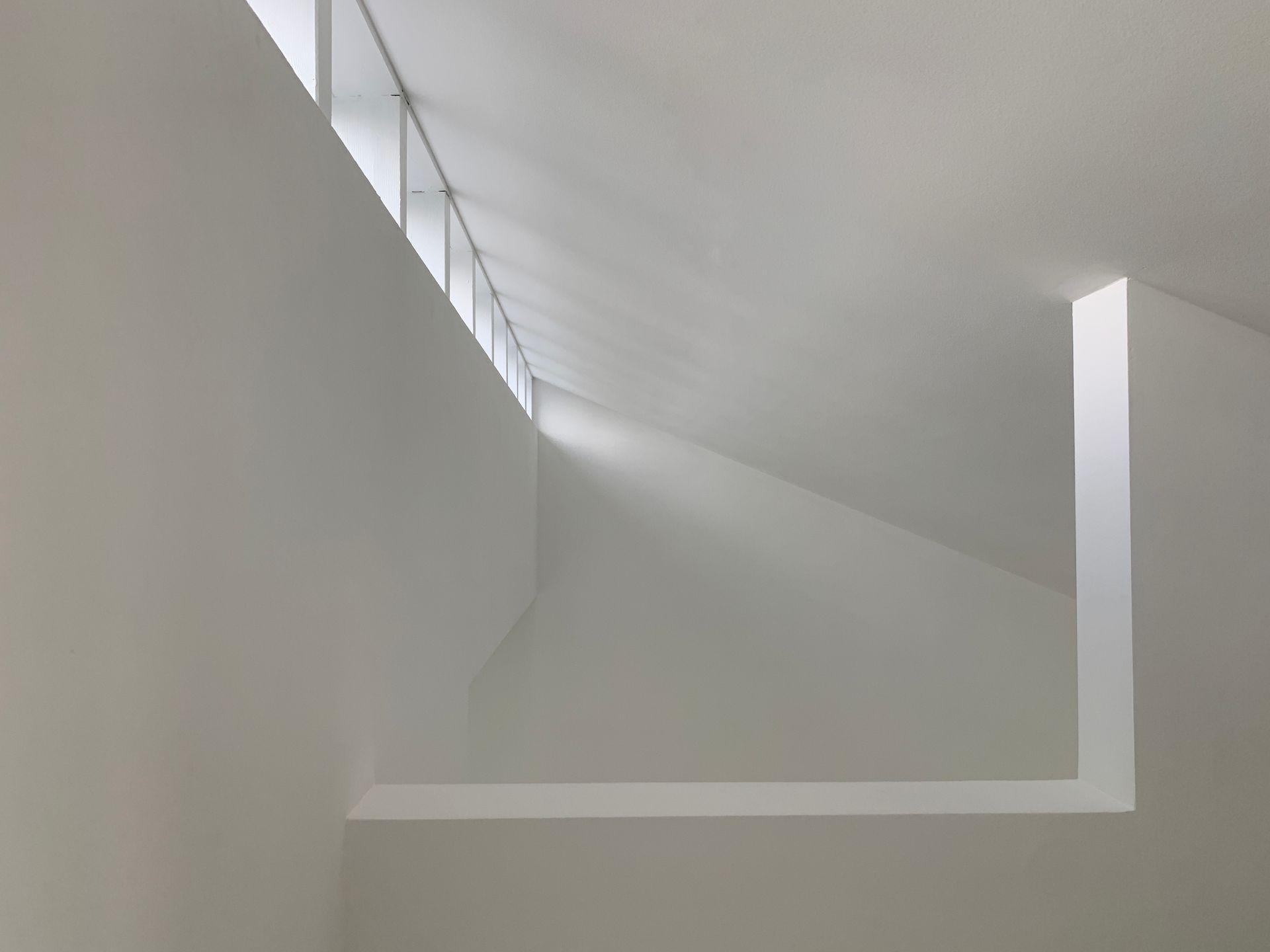 Minimalistisches weißes Interieur mit schräger Decke und einer Reihe von Fenstern entlang der oberen linken Kante.