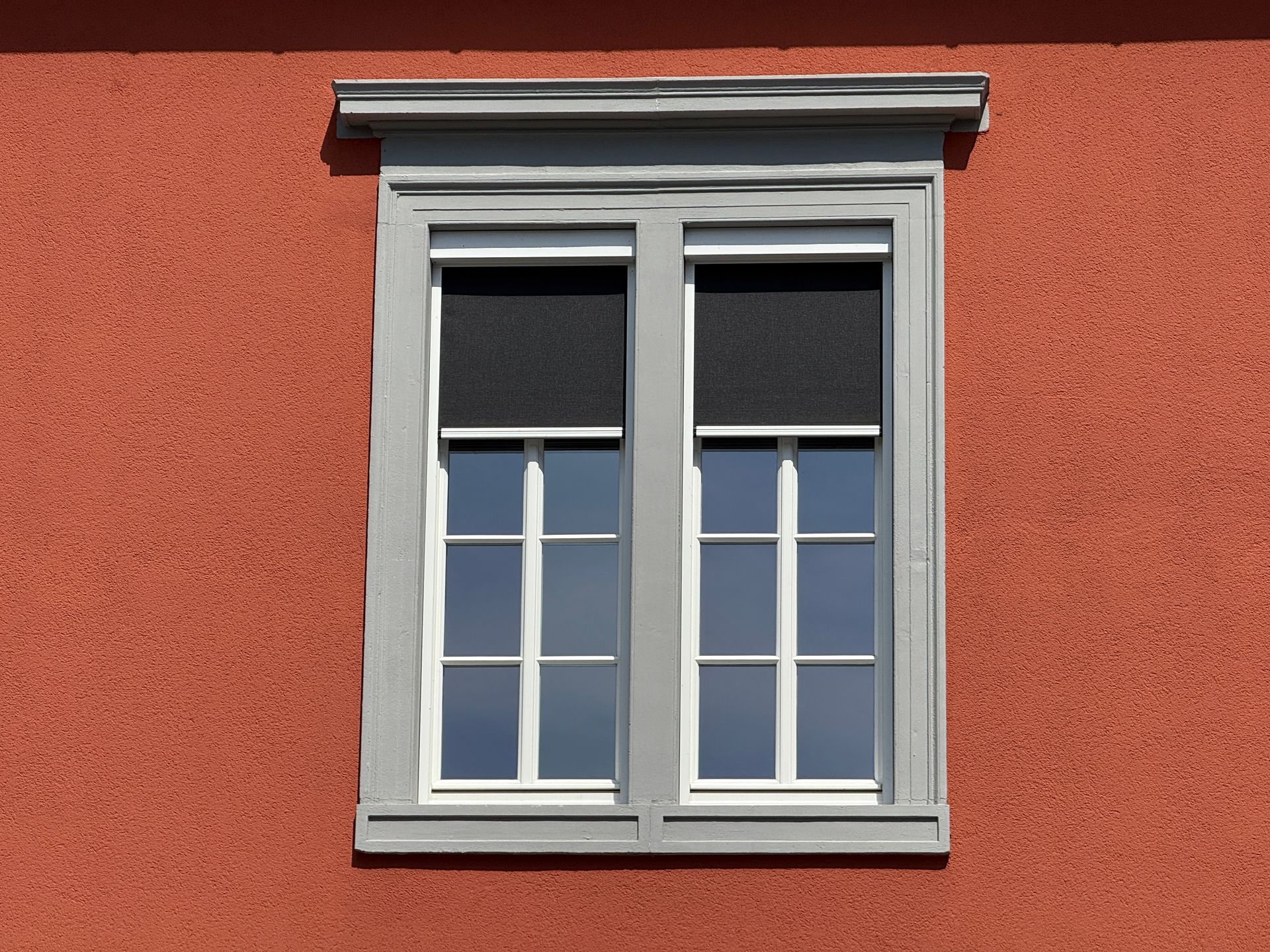 Ein doppelt verglastes Fenster mit grauem Rahmen und schwarzen Jalousien, eingelassen in eine strukturierte, 