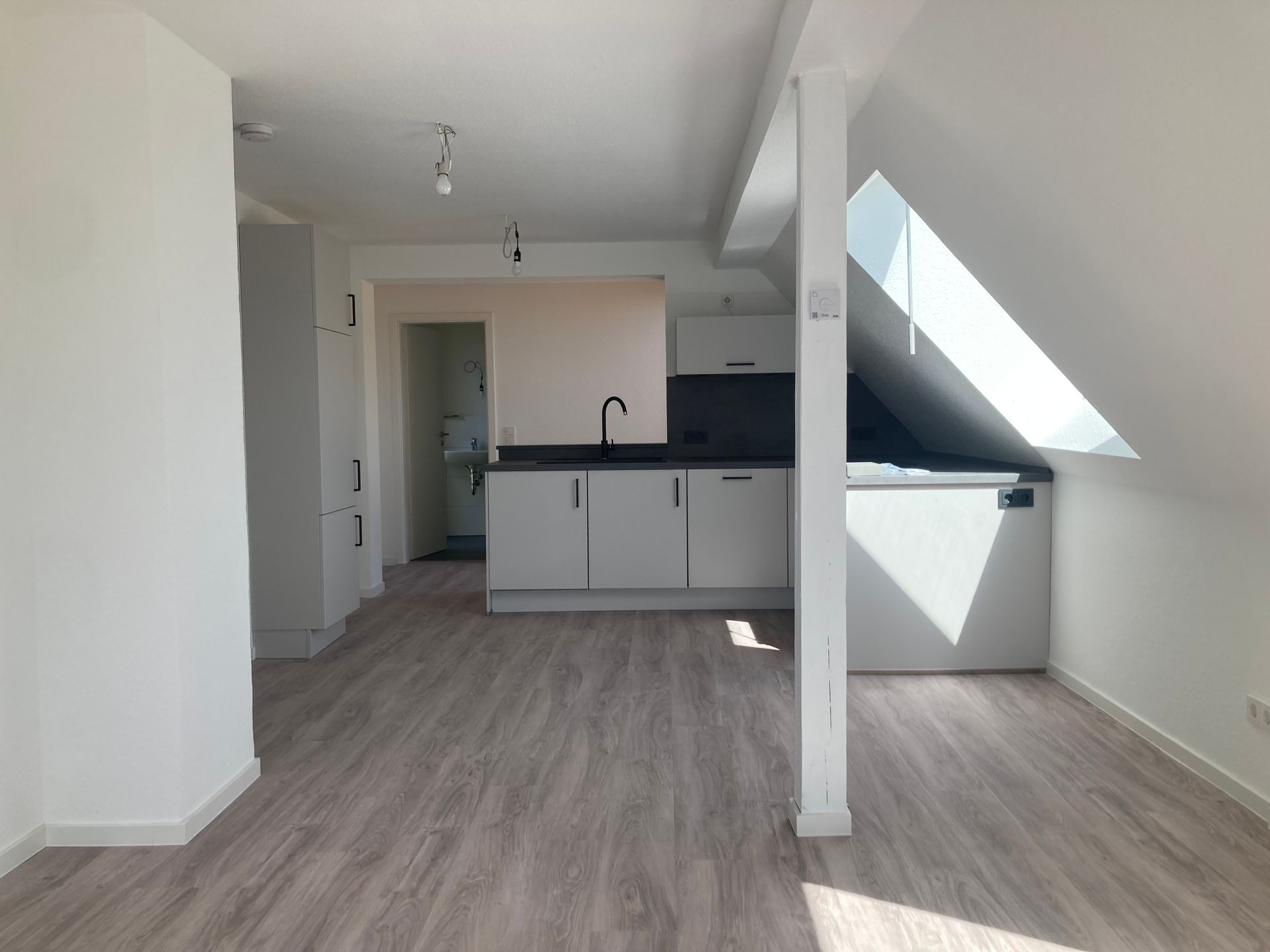 Eine moderne Küche mit hellgrauen Schränken, Holzbodenoptik und einer Dachschräge mit Oberlicht in einer Dachgeschosswohnung.