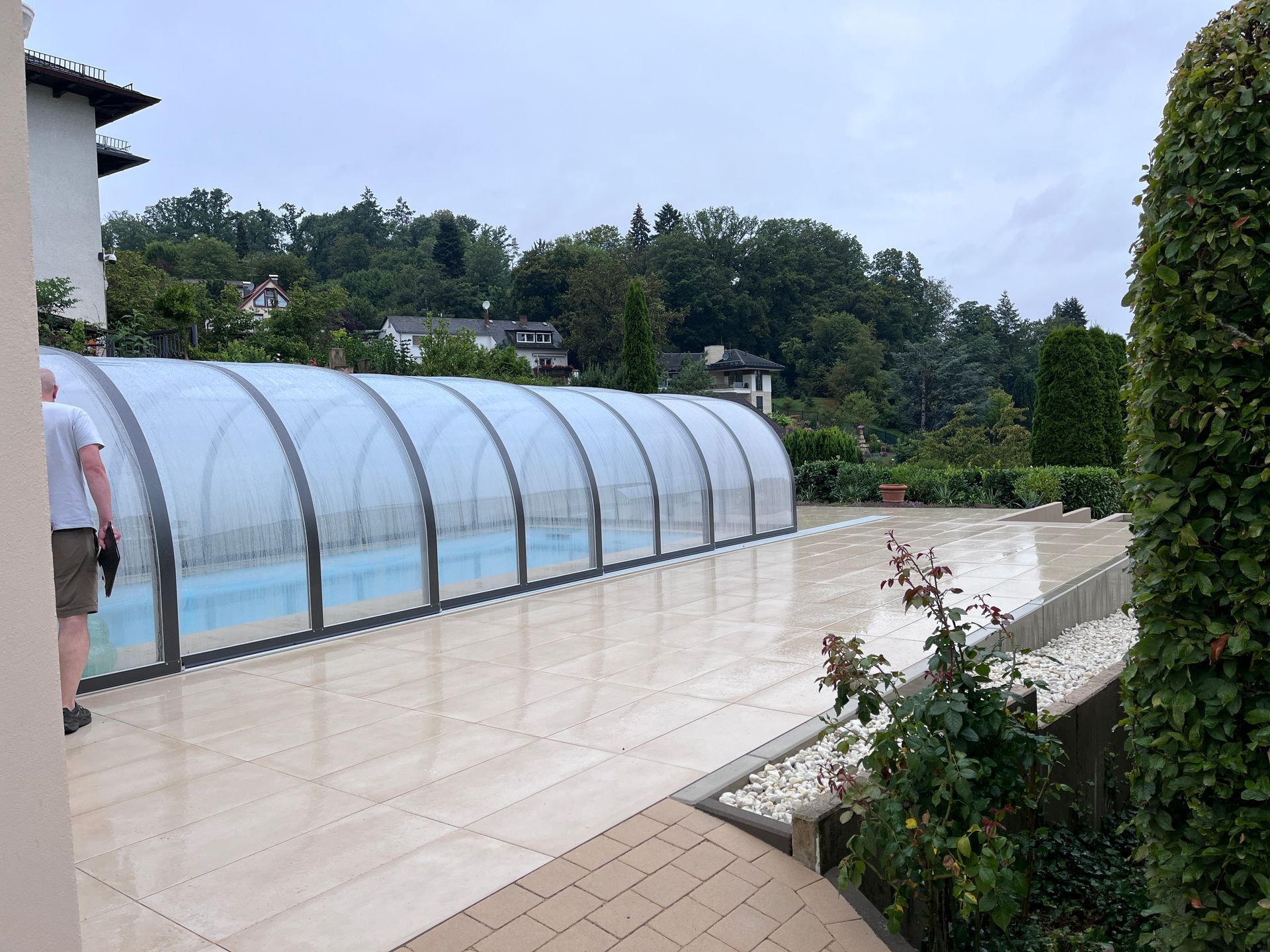 Eine Person steht auf einer Terrasse neben einem Außenpool, der von einer lichtdurchlässigen, bogenförmigen 