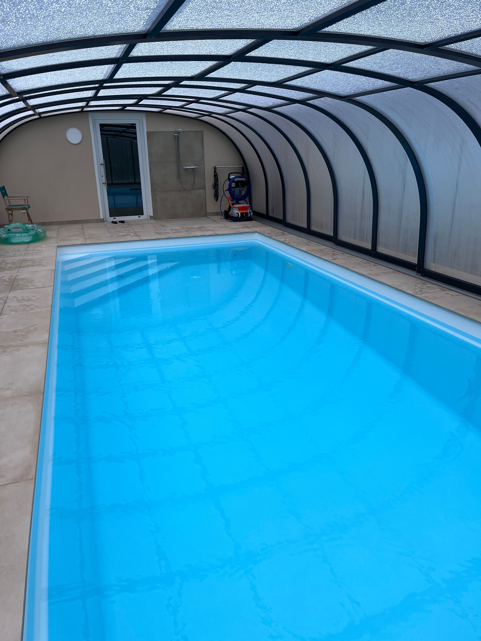 Ein rechteckiges Hallenbad mit leuchtend blauem Wasser, untergebracht in einer gebogenen, lichtdurchlässigen, 