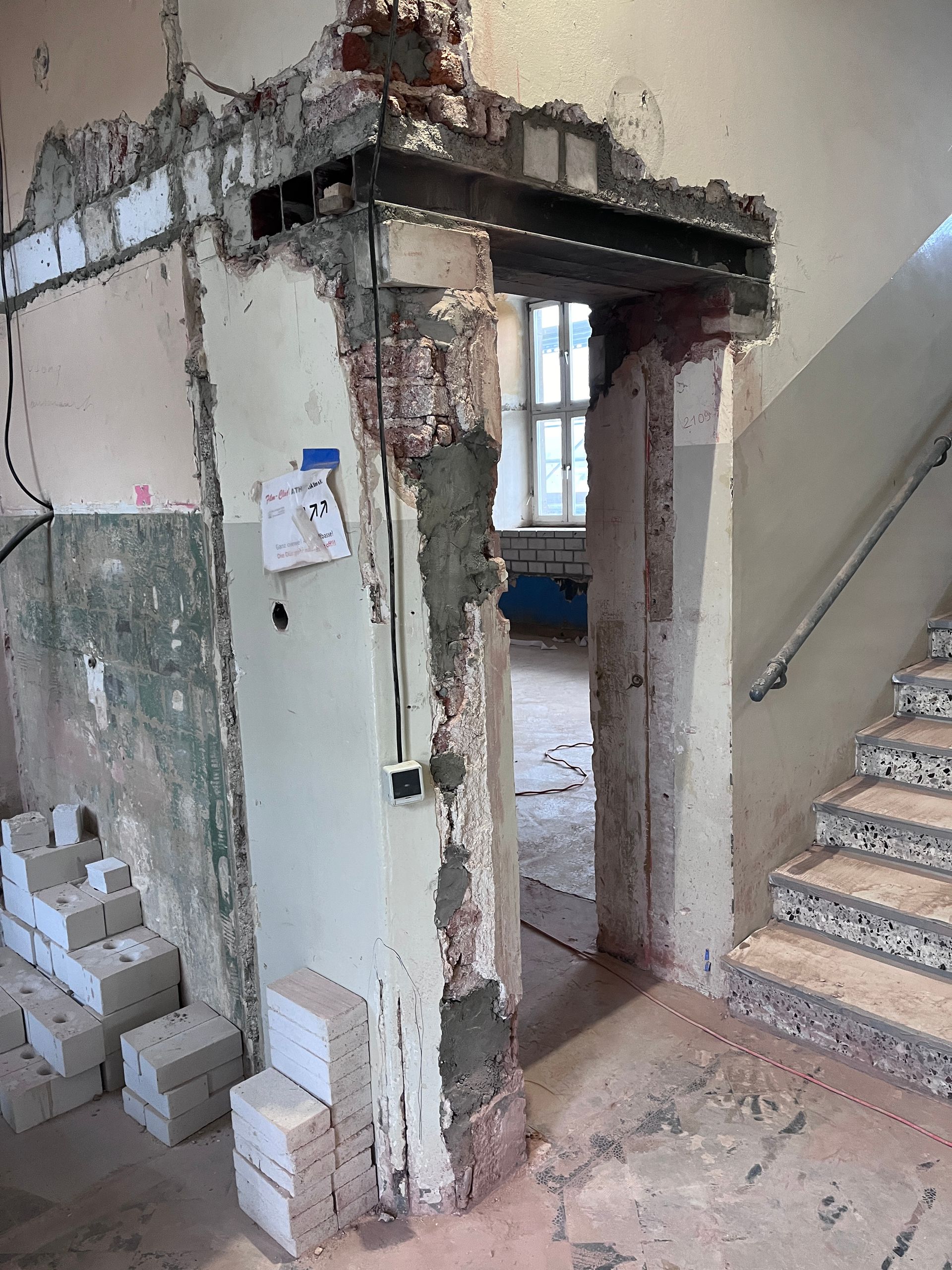 Eine Baustelle mit einem Türrahmen aus freiliegendem Stahl, teilweise abgerissenen Wänden und einer nahegelegenen Treppe.