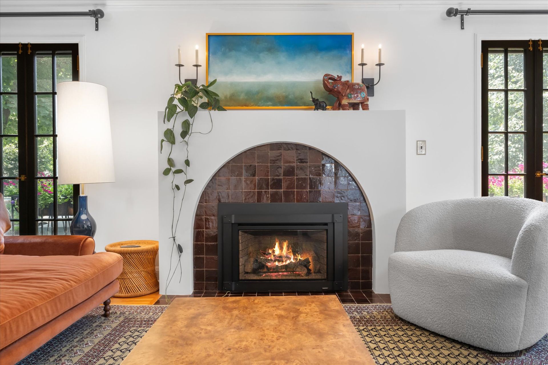 A living room with a brown tiled arched fireplace, a white sofa, and a gray armchair centered on a patterned rug.