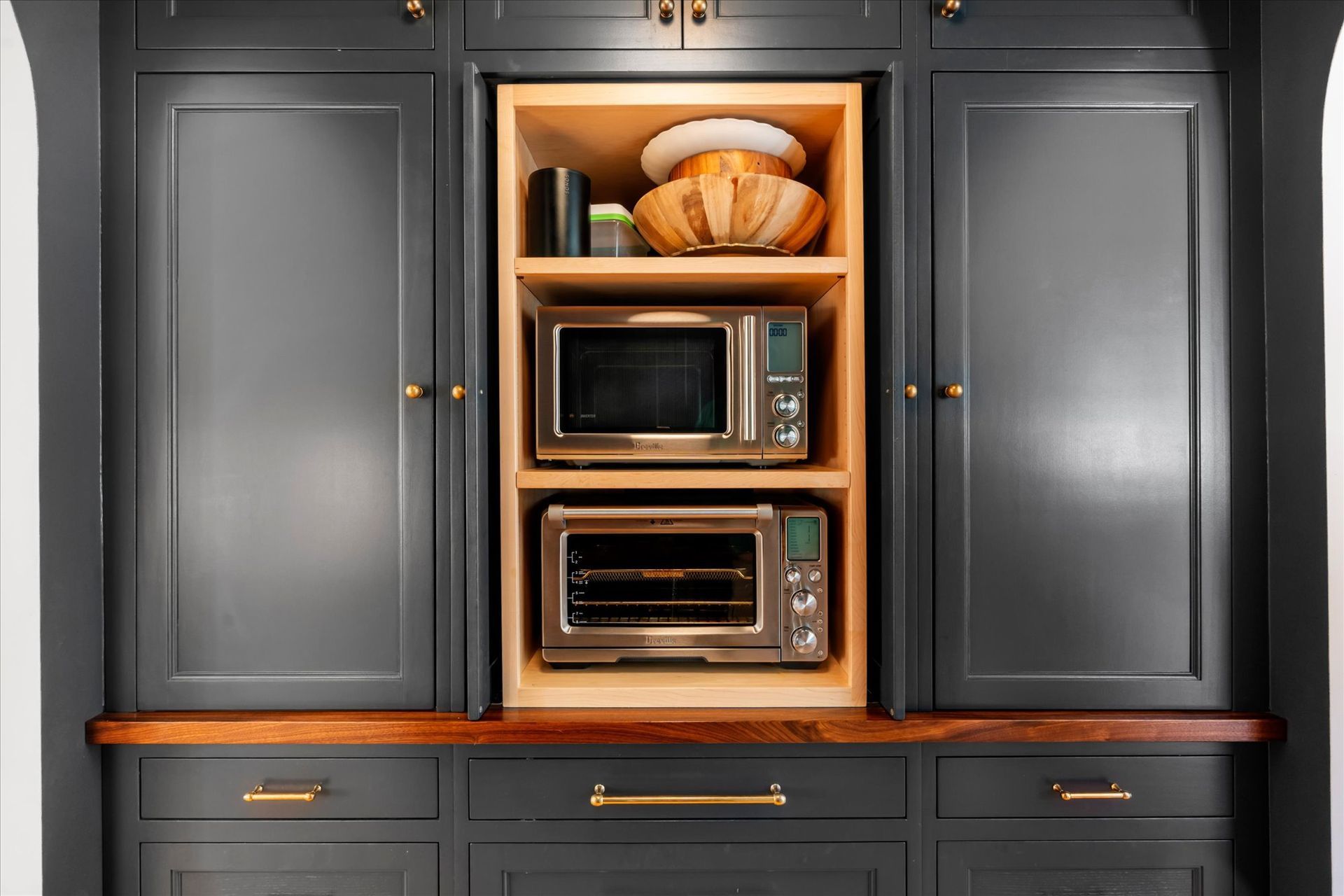 A custom kitchen cabinet in dark gray, featuring a central wood-lined niche housing a microwave and toaster oven.
