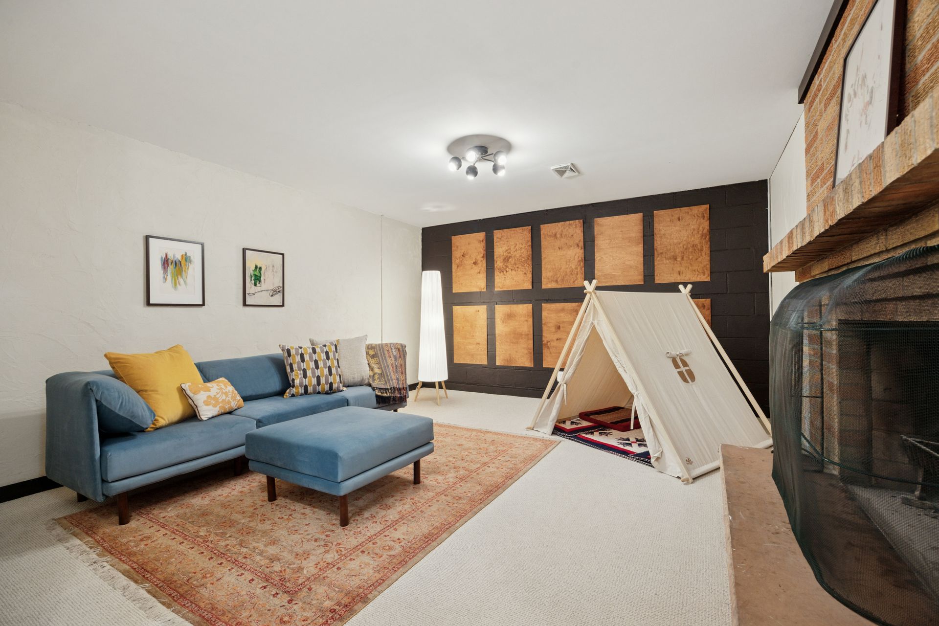 A cozy room featuring a blue sofa, an area rug, and a play tent set up on the floor near a large brick fireplace.