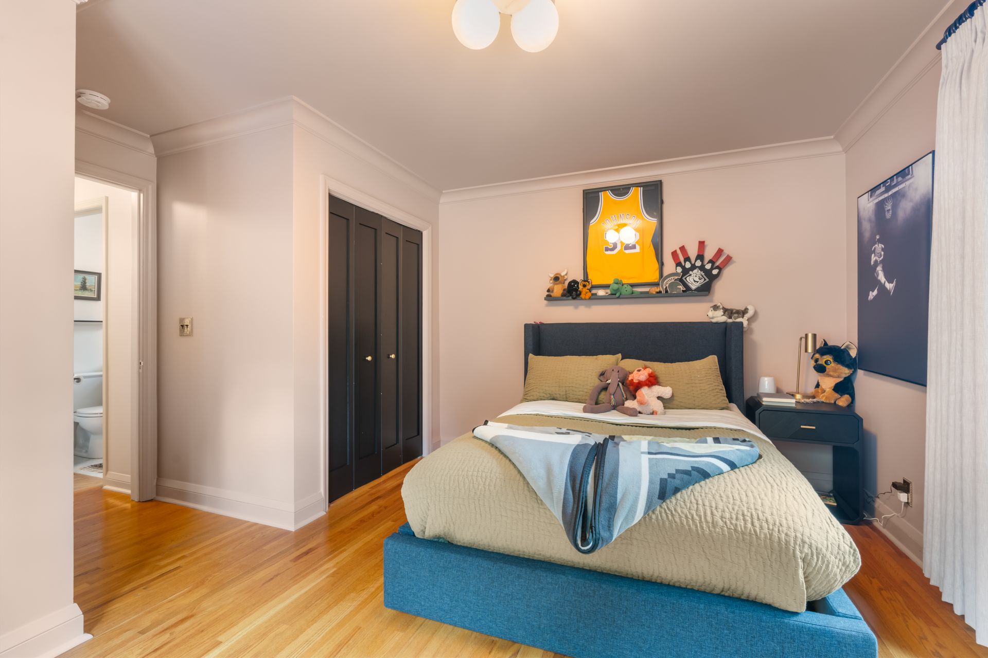 A cozy bedroom with a blue platform bed, light pink walls, dark wood closet doors, and wood floors.